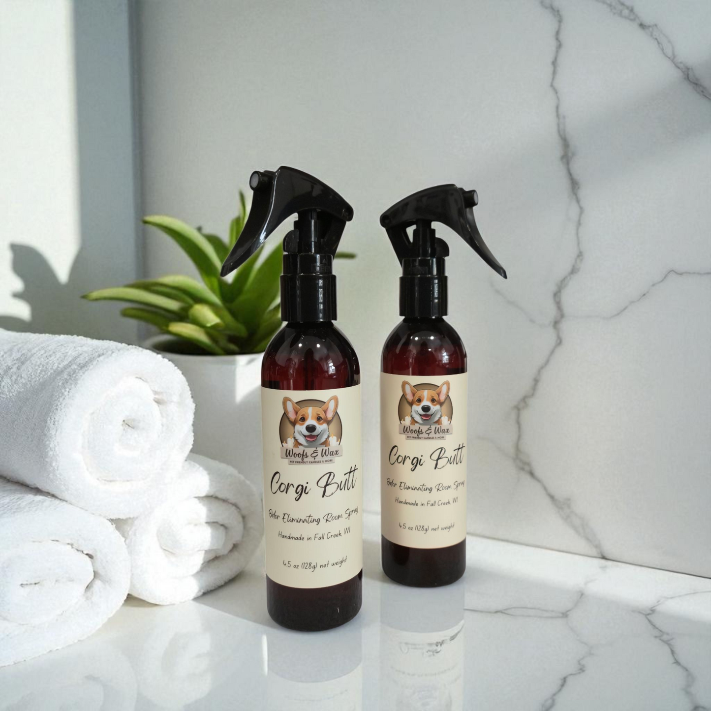 Two bottles of 'Corgi Butt' room spray on a marble surface with towels and a plant in the background.