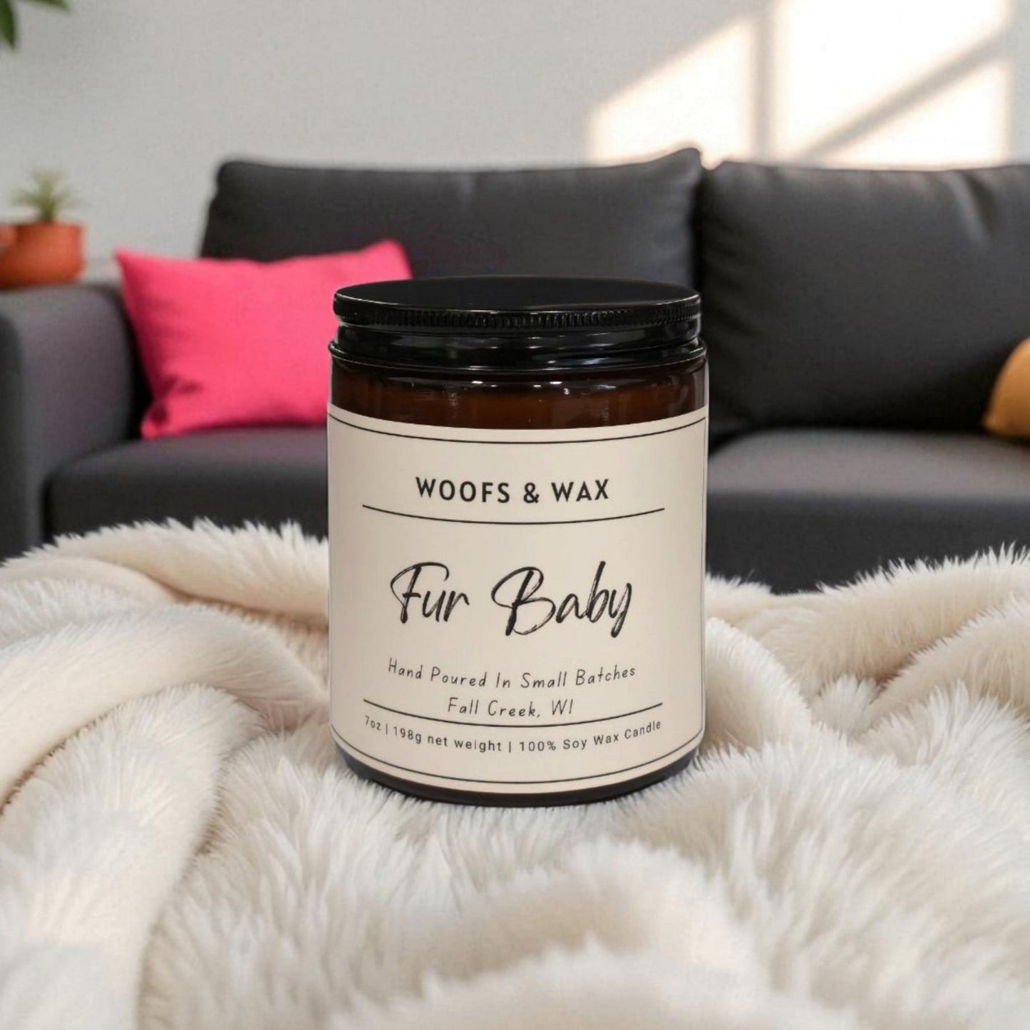 Candle jar labeled 'Woofs & Wax Fur Baby' on a fluffy blanket with a couch in the background