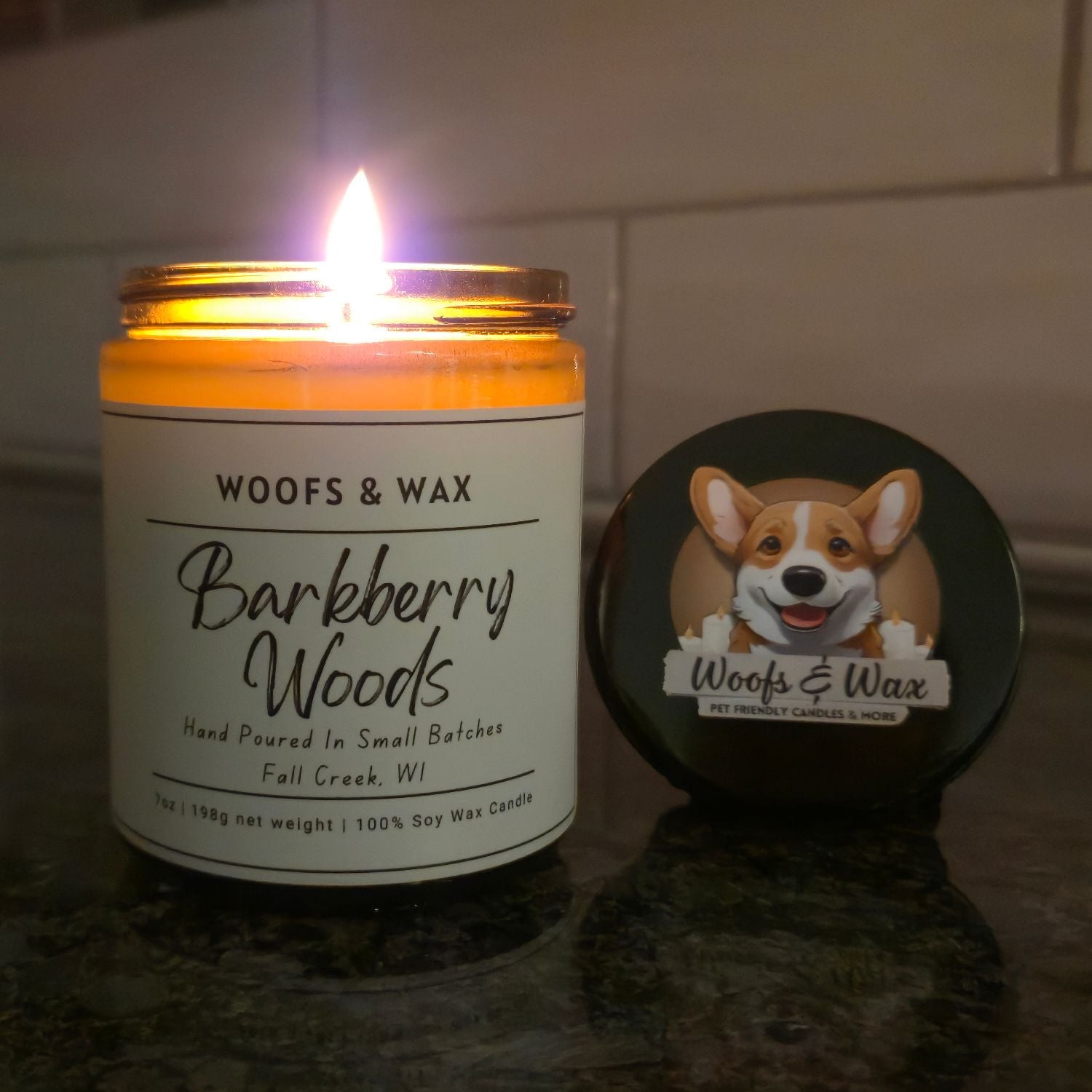 Candle labeled 'Woofs & Wax Barkberry Woods' with a coaster featuring a dog illustration on a reflective surface.