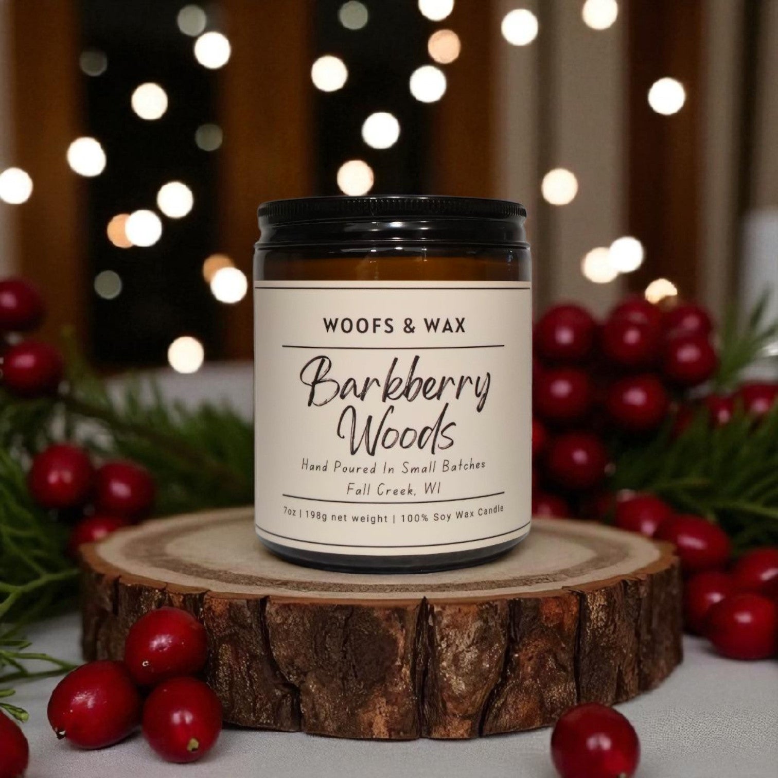 Candle labeled 'Barkberry Woods' by 'Woofs & Wax' on a wooden stand with berries and lights in the background.