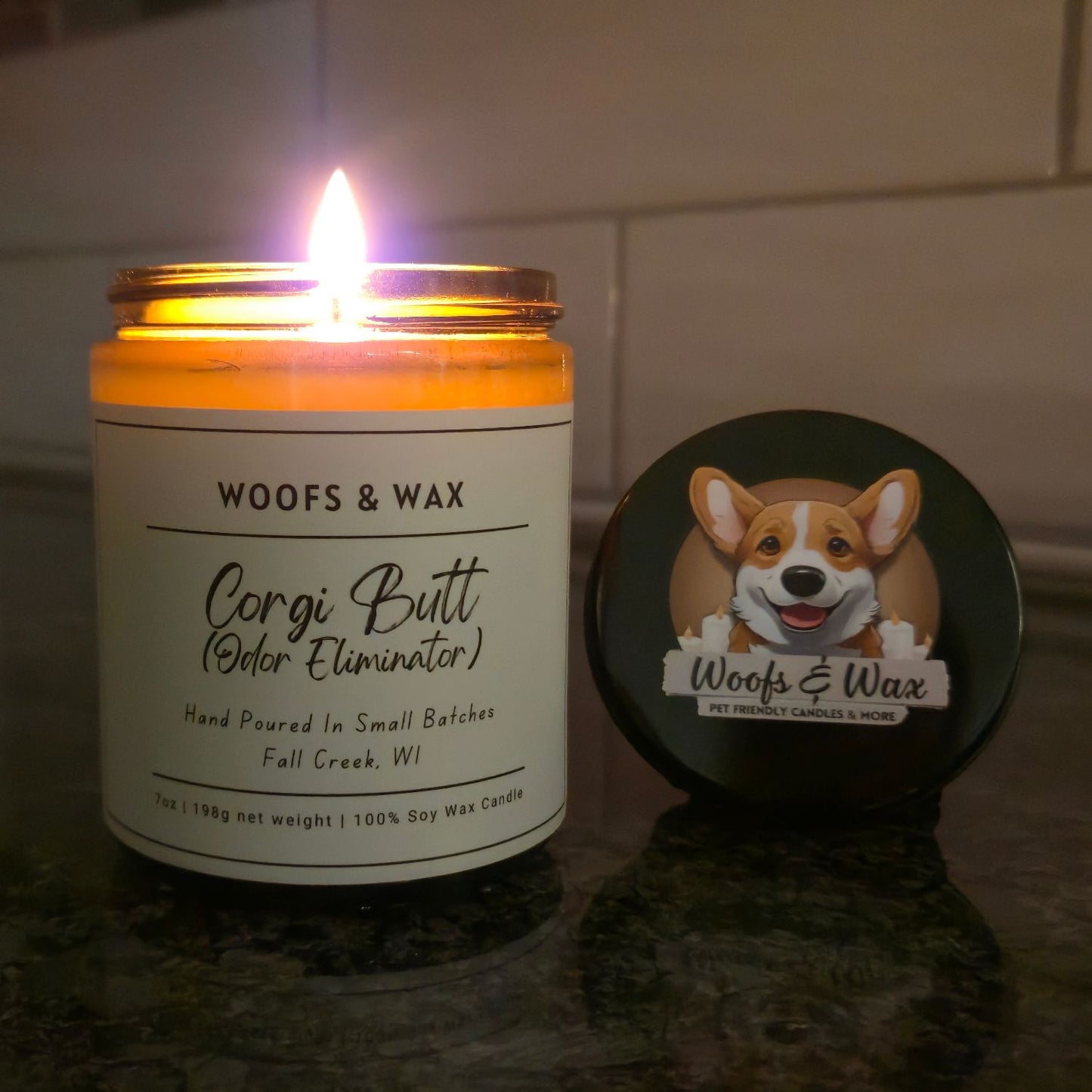 Candle labeled 'Woofs & Wax' with a lit flame on a reflective surface.