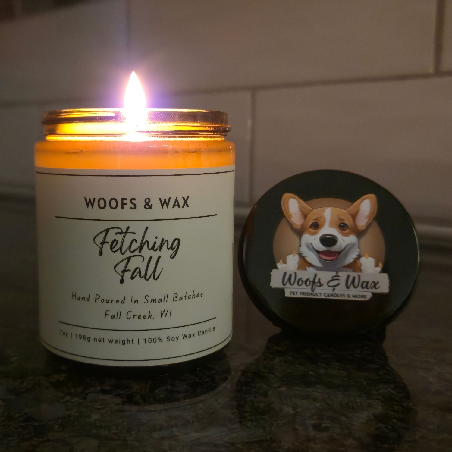 Candle labeled 'Woofs & Wax Fetching Fall' with a dog illustration on a dark surface.