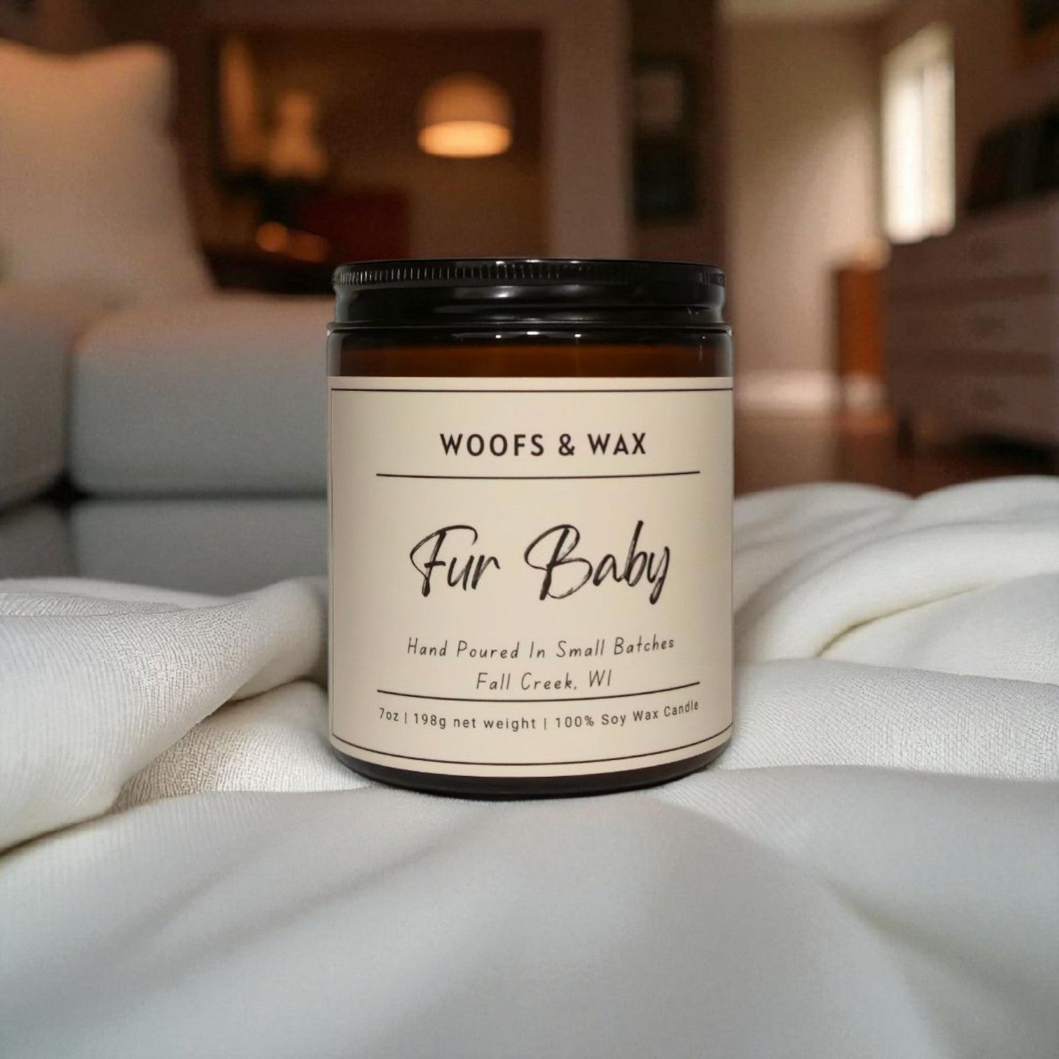 Candle jar labeled 'Woofs & Wax Fur Baby' on a white surface with a blurred indoor background