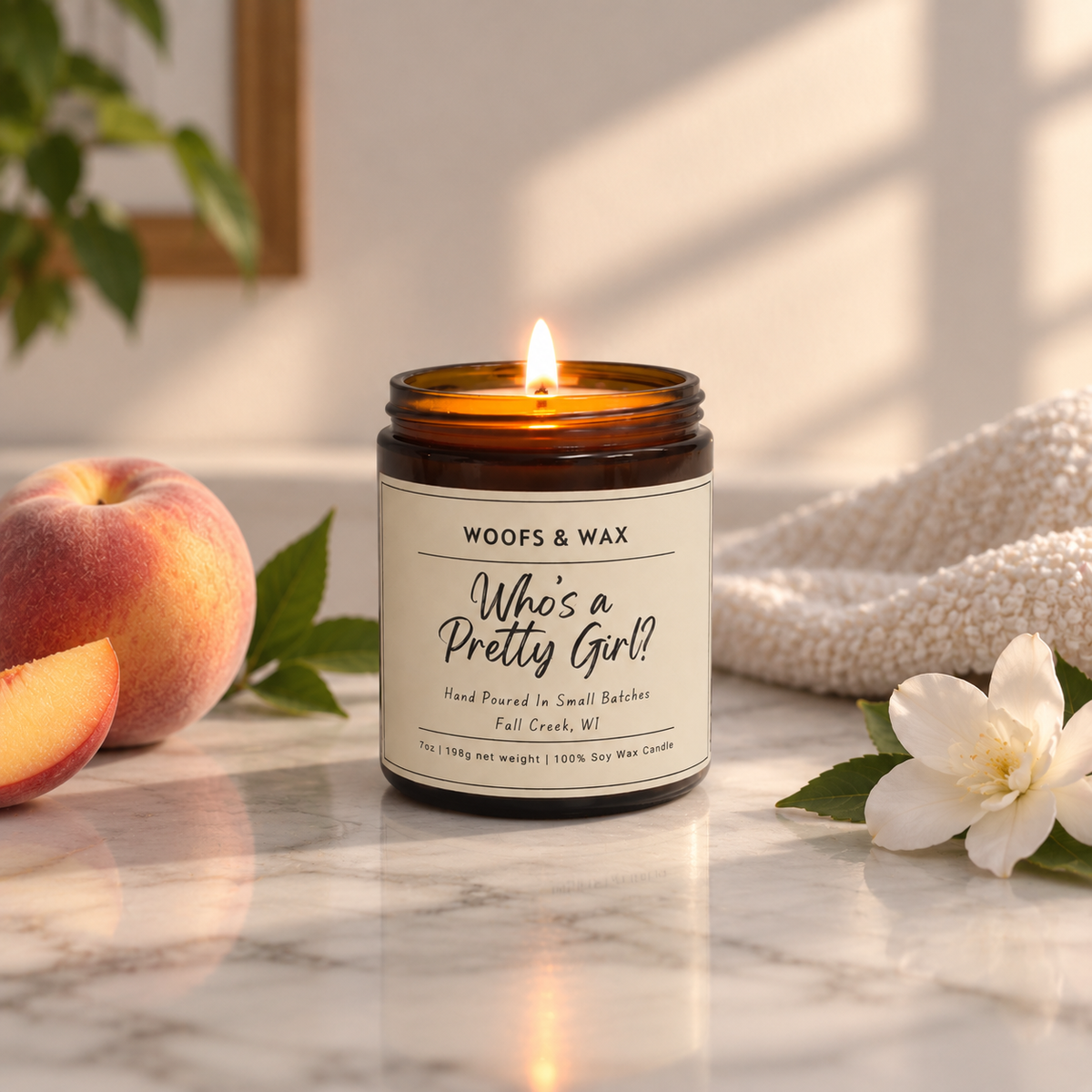 An amber glass jar candle with a lit flame sits on a marble surface. The label reads 'WOOFS & WAX Who's a Pretty Girl?'.