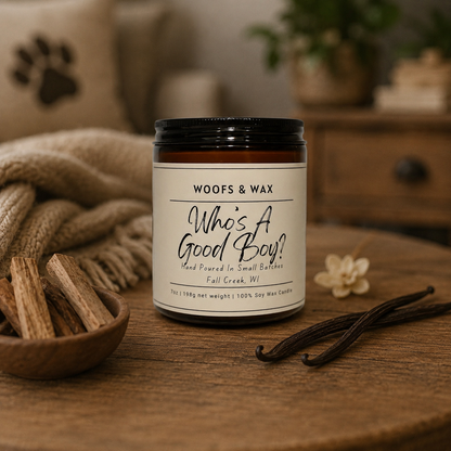 Candle labeled 'Woofs & Wax Who's A Good Boy?' on a wooden surface with cinnamon sticks and vanilla beans.