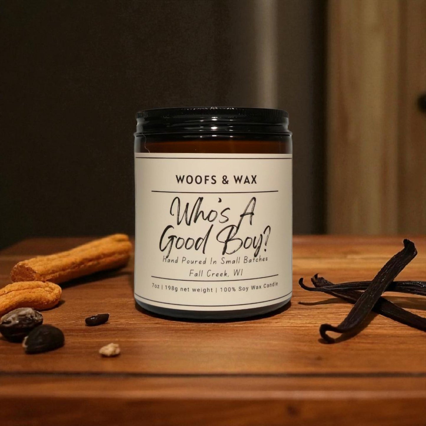 Candle jar labeled 'Woofs & Wax Whos A Good Boy?' on a wooden surface with vanilla beans and chocolate.