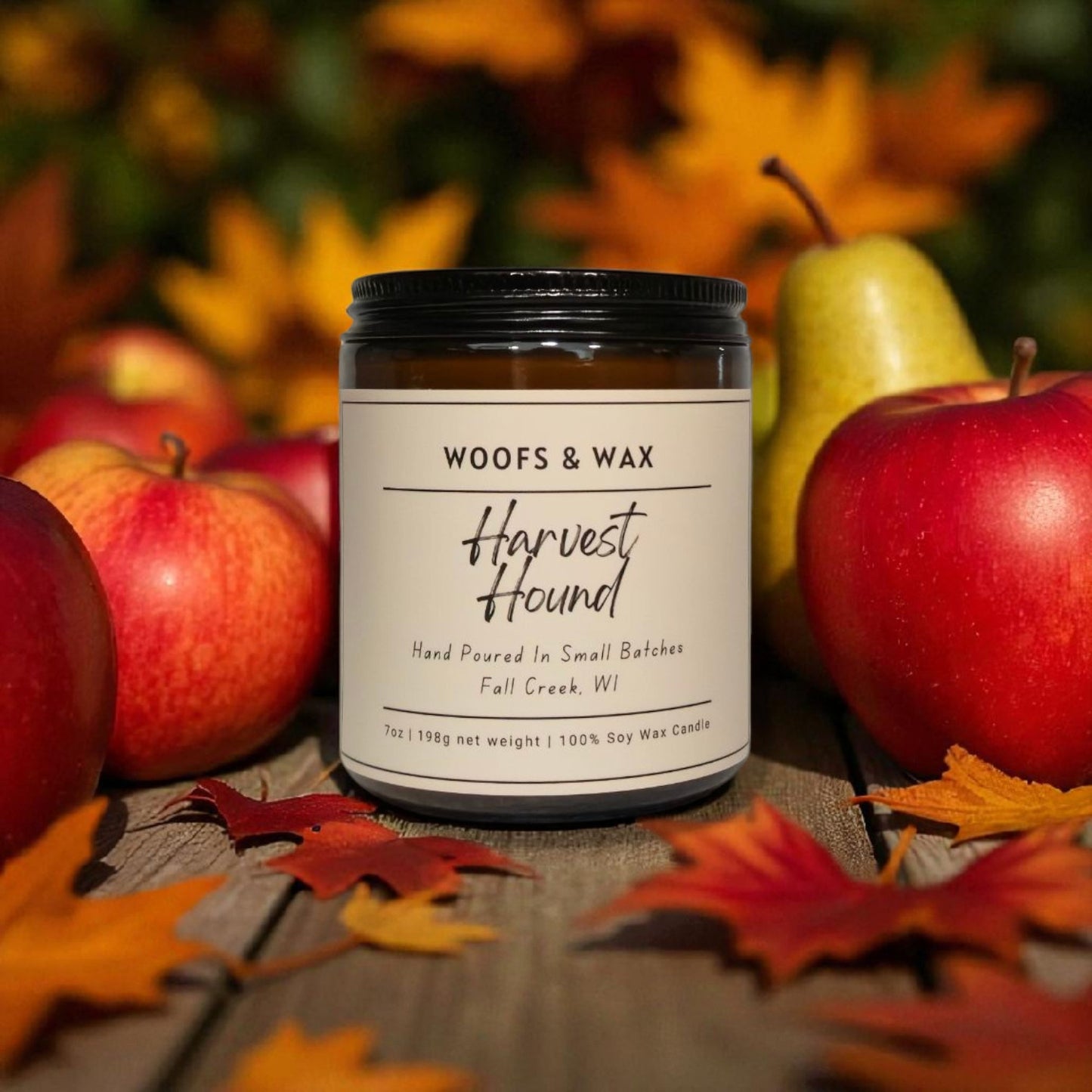 Candle jar labeled 'Woofs & Wax Harvest Hound' surrounded by apples and leaves on a wooden surface.