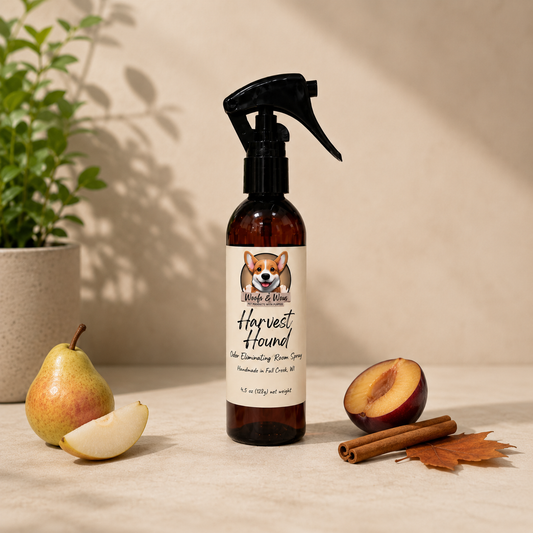 Brown spray bottle with a label featuring a dog illustration, surrounded by a pear, half-peeled pear, pluot, cinnamon stick, and leaf on a neutral background.