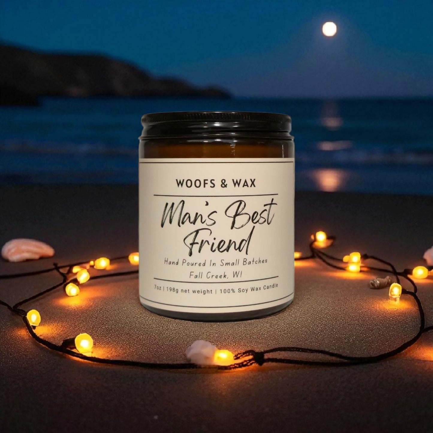 Candle jar labeled 'Man's Best Friend' by Woofs & Wax on a beach at night with string lights.