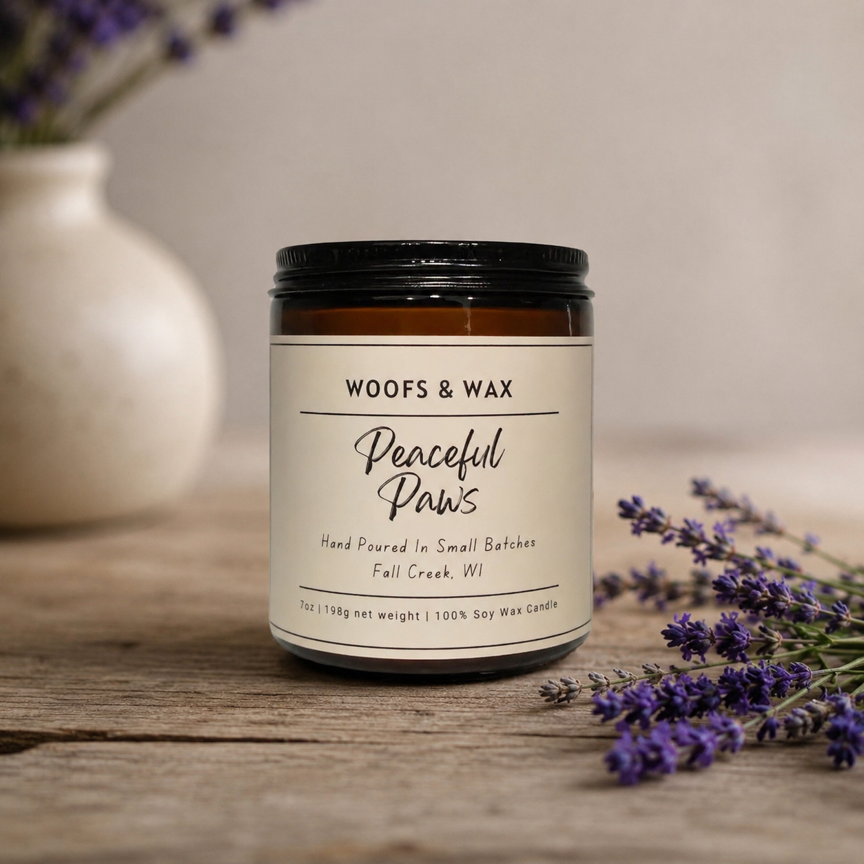 Candle jar labeled 'Woofs & Wax Peaceful Paws' on a wooden surface with lavender flowers.