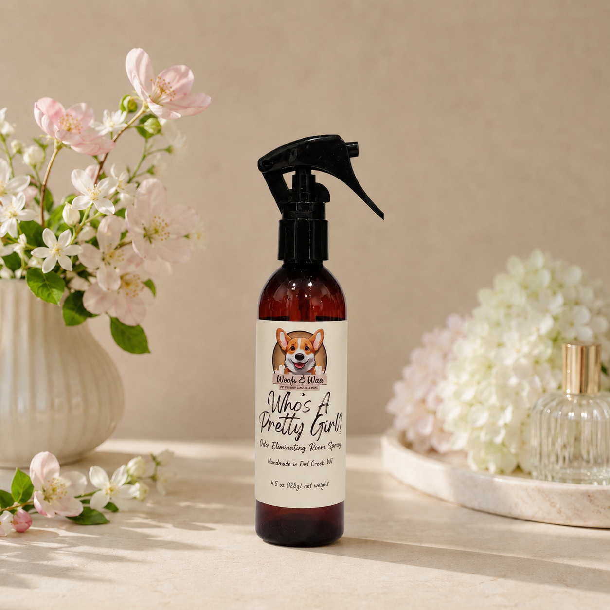 Spray bottle labeled 'Who's a Pretty Girl' with flowers and perfume in the background