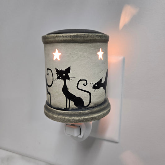Electric plug in wax warmer with black cats and stars plugged into an electrical outlet on a wall.