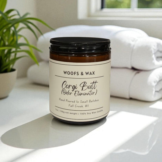 Candle jar labeled 'Woofs & Wax' on a white surface with a plant and towels in the background