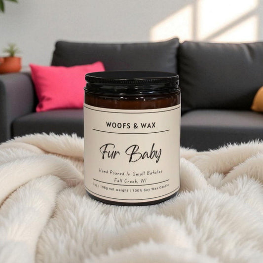 Candle jar labeled 'Woofs & Wax Fur Baby' on a fluffy blanket with a couch in the background
