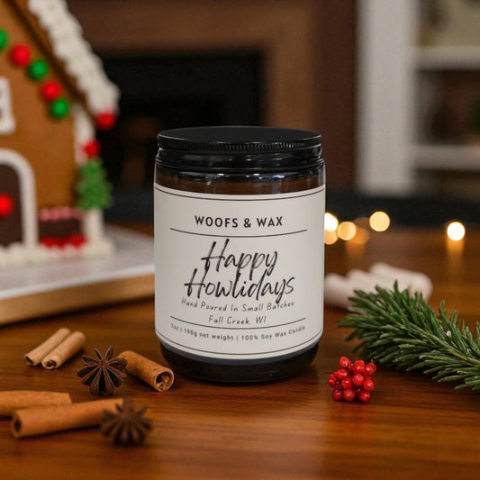 Candle labeled 'Woofs & Wax Happy Howlidays' on a wooden surface with festive decorations.