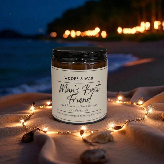 Candle labeled 'Man's Best Friend' on a beach at night with string lights and ocean view.