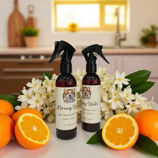 Two bottles of 'Morning Walks' room spray with flowers and oranges on a kitchen counter.